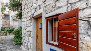 A stone building with a wooden door and window, a sign indicating it is an apartment, and a small garden area. - Dalmatian Cottage, Pedestrian Zone (Split)