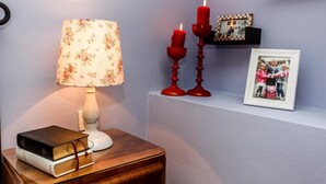 A bedside table with a lamp, books, two red candles, and a framed photo on a shelf. - Dalmatian Cottage, Pedestrian Zone (Split)