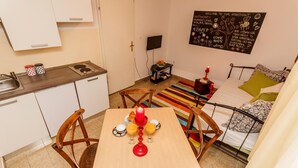 A compact living space with a kitchenette, a dining area with a table set for two, a bed with patterned bedding, and a colorful striped rug. - Dalmatian Cottage, Pedestrian Zone (Split)