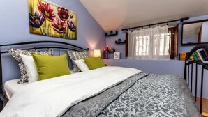 A bedroom with a bed, a painting of flowers, a window with curtains, and a bedside table with a lamp. - Dalmatian Cottage, Pedestrian Zone (Split)