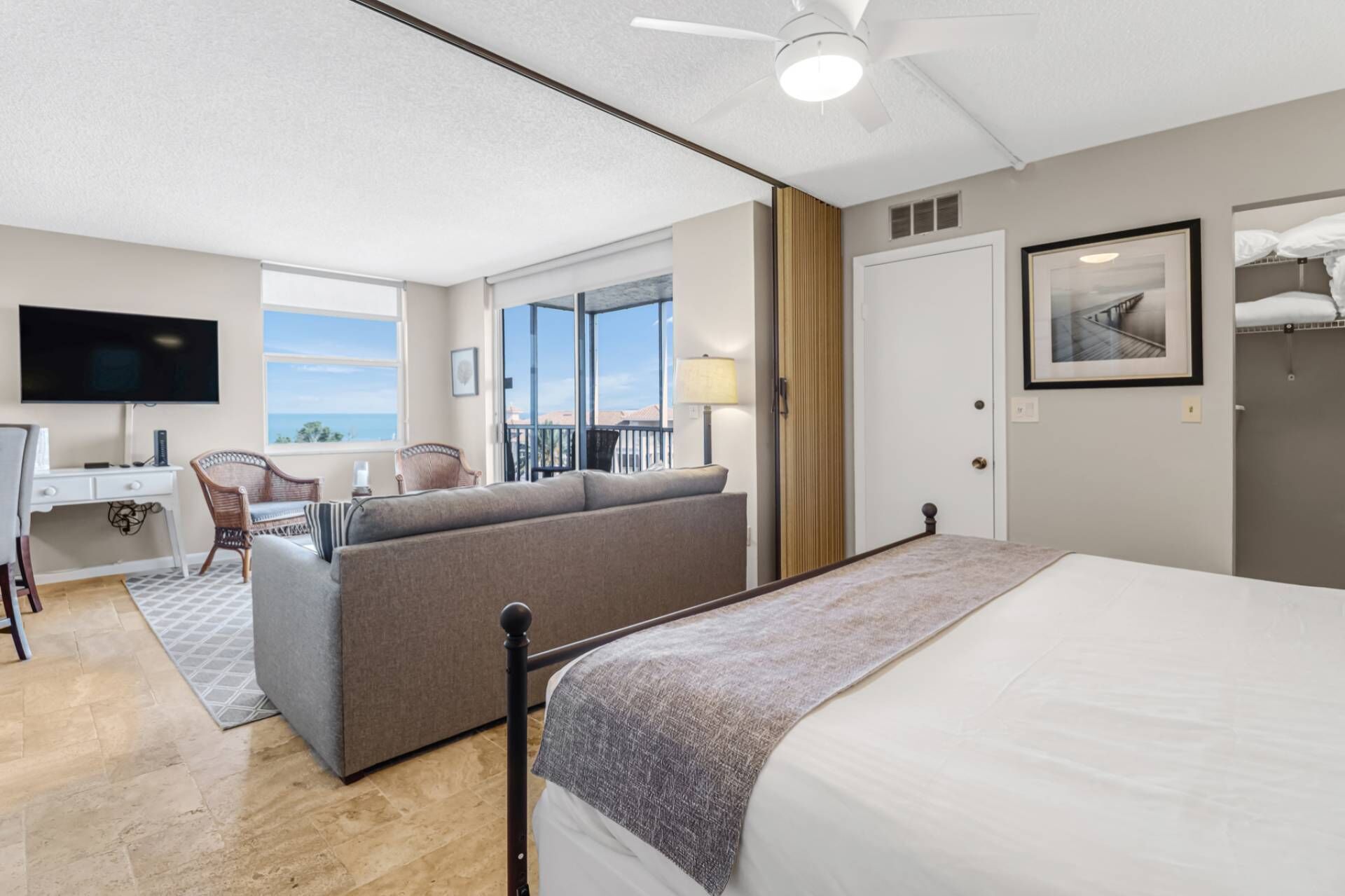 A hotel room with a bed, a desk with a TV, a sofa, and a balcony with a view.