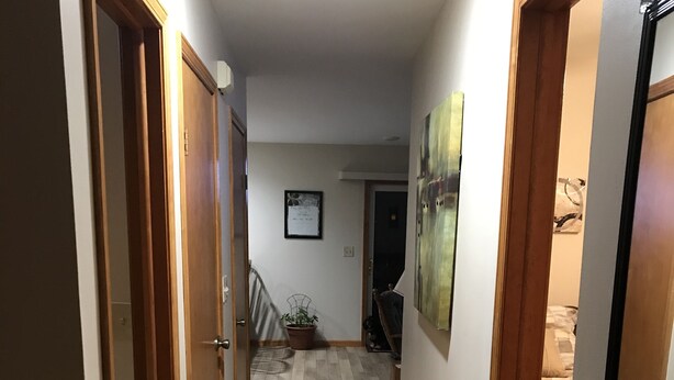 Un pasillo estrecho con puertas de madera a ambos lados, una alfombra estampada en el suelo y una escalera al final.