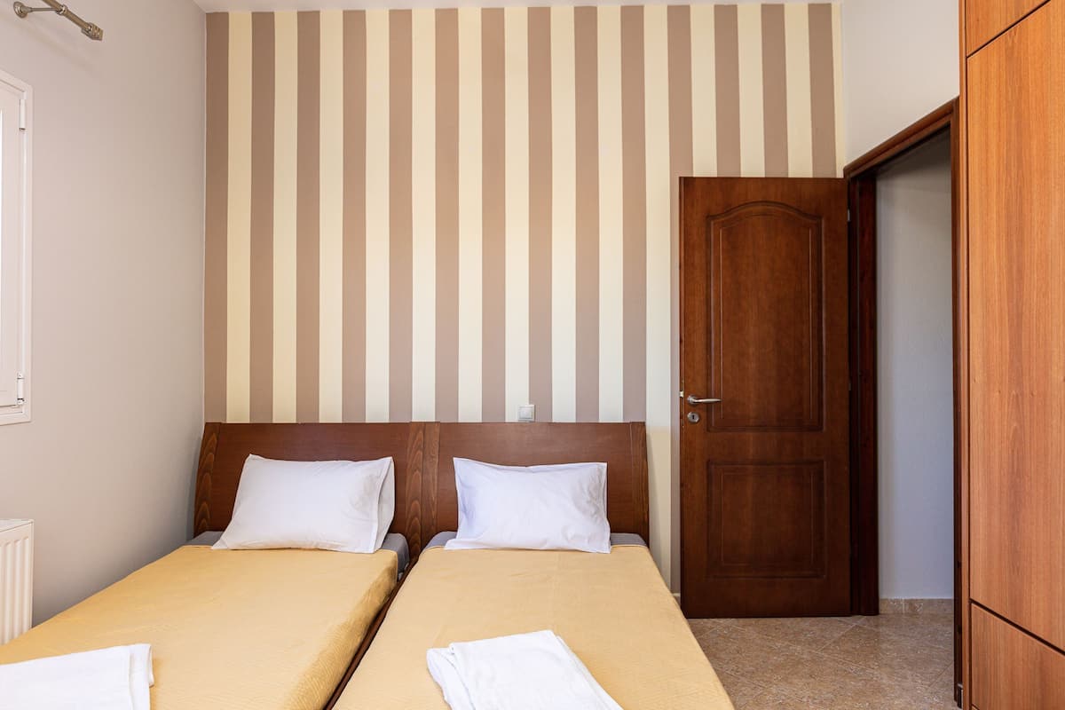 A hotel room with two single beds, a wooden door, and a striped wall.