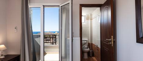 A hotel room with a bed, a bathroom with a toilet and sink, and a balcony with a view of the sea.