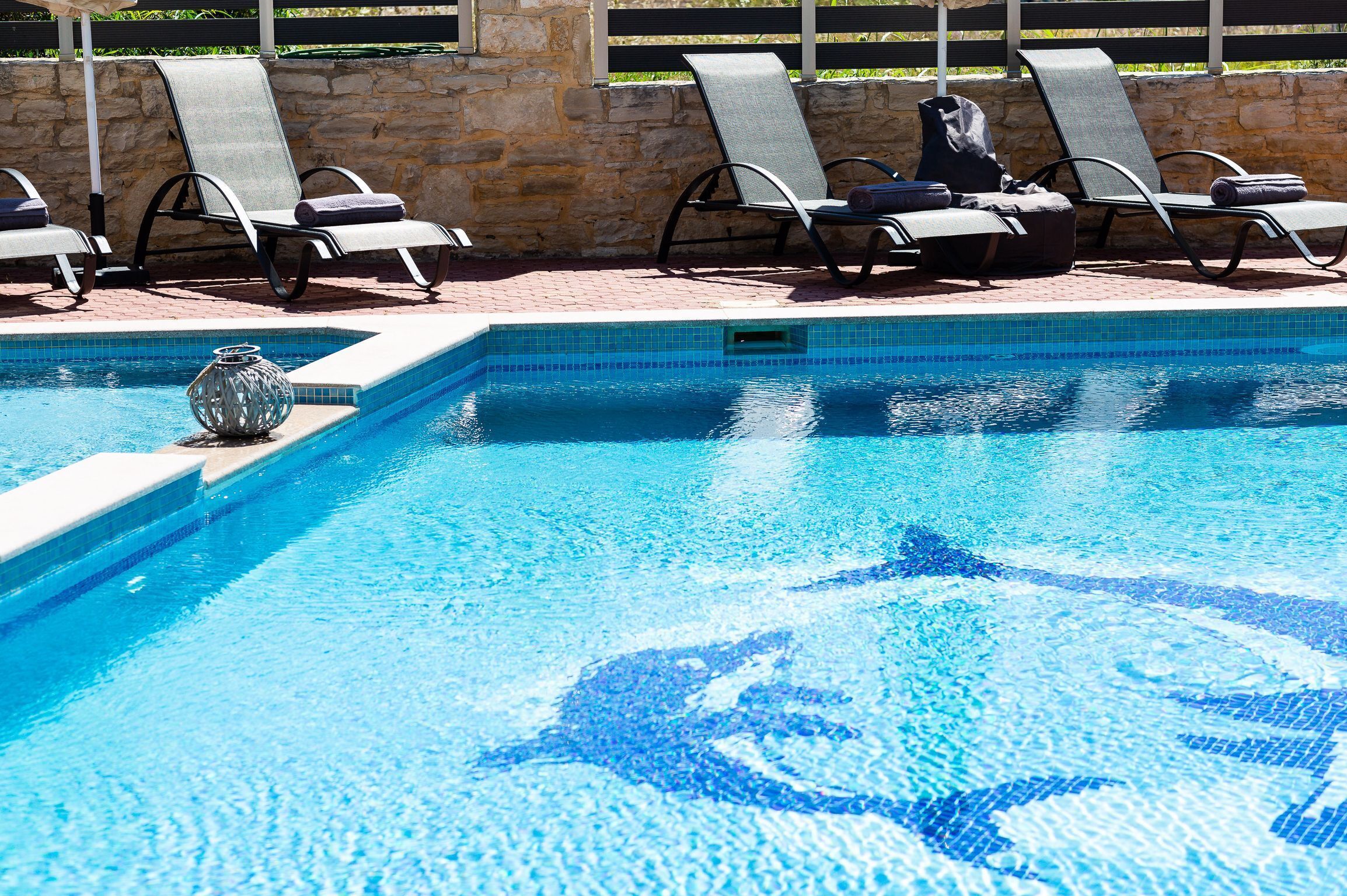 A swimming pool with lounge chairs and a stone wall.