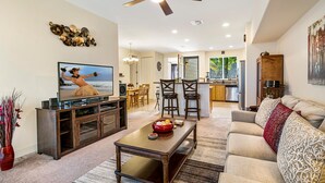 A modern living room with a television, a dining area, and a kitchen.