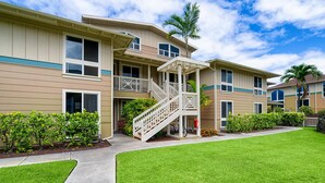 A multi-story residential building with a covered porch, a staircase, and a well-maintained lawn.