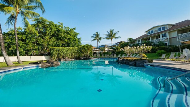A swimming pool with clear blue water, surrounded by palm trees and a building with balconies.