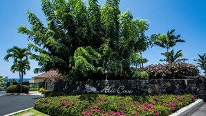 A stone wall with the name "Alii Cove" and a lush garden with pink flowers.