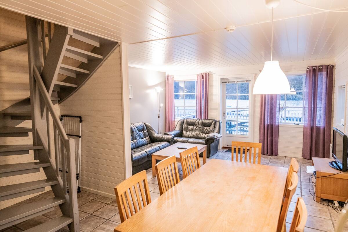 A spacious living area with a wooden dining table, a sofa, and a staircase.