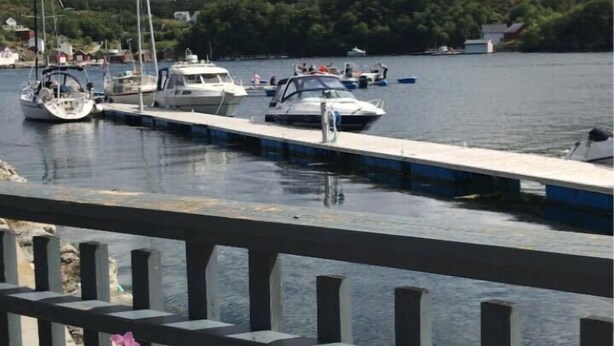 A marina with boats docked, a wooden deck, and a flower bed with purple flowers. - Knarren Brygge (Hitra)