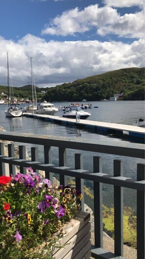 Un puerto deportivo con barcos amarrados, una cubierta de madera y un parterre con flores púrpuras.