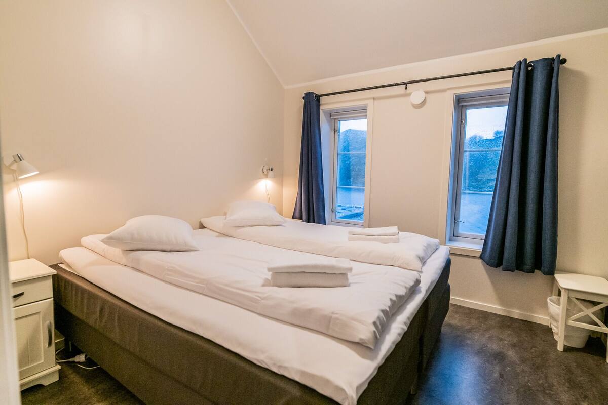 A bedroom with a bed, bedside tables, a lamp, and a window with curtains.