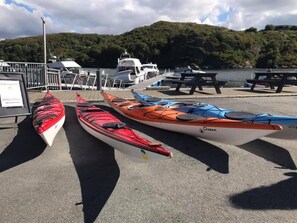 Tres kayaks alineados en un muelle, con una montaña y barcos al fondo.