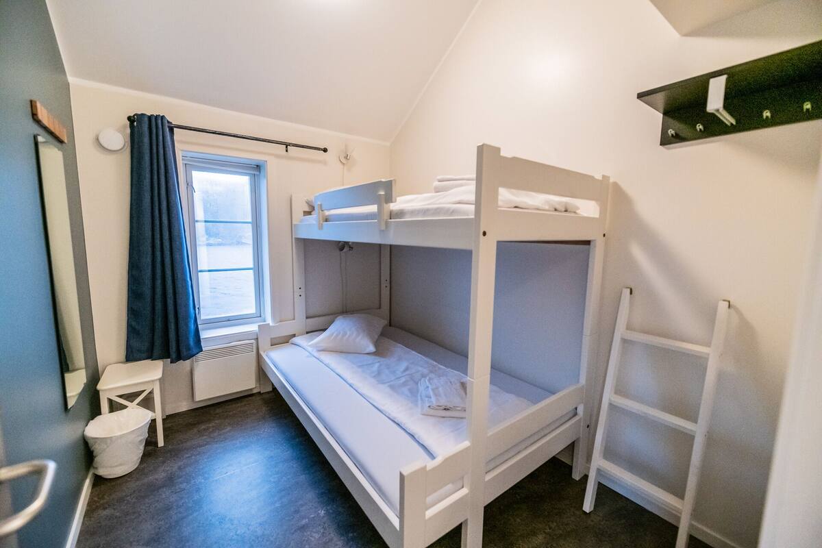 A bunk bed room with a window, a small table, and a ladder.