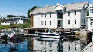 A marina with boats docked, a white building with a sloped roof, and a clear blue sky. - Knarren Brygge (Hitra)
