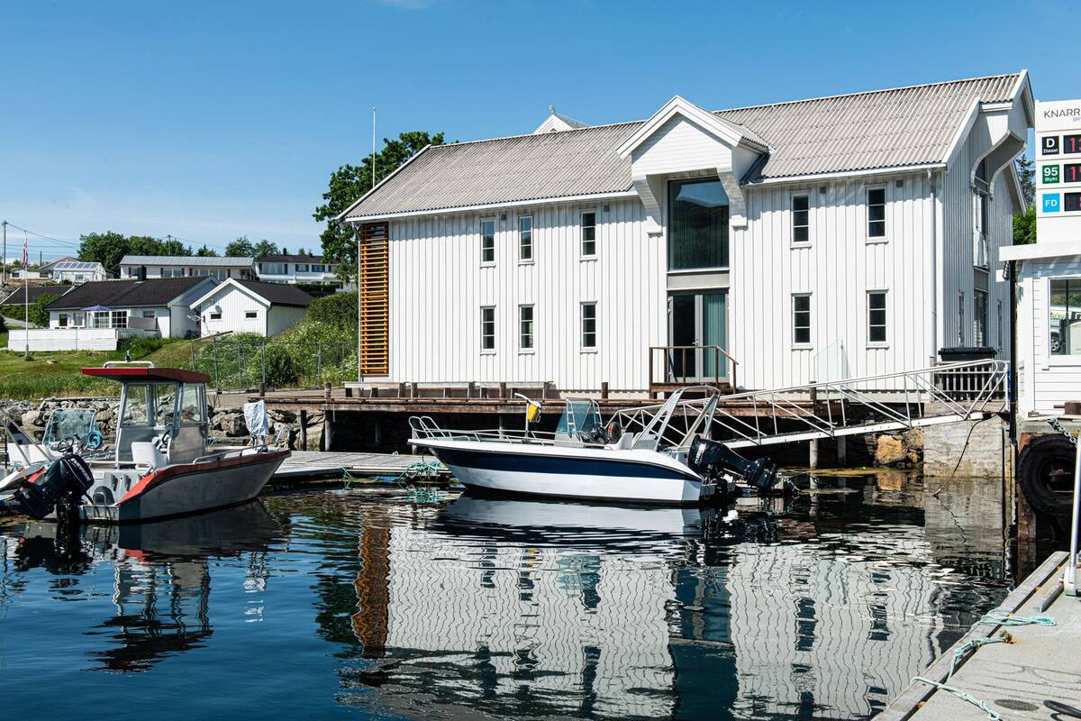 A marina with boats docked, a white building with a sloped roof, and a clear blue sky.
