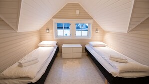 A small, triangular attic bedroom with two single beds, a small table, and a window providing a view of the outside. - Knarren Brygge (Hitra)