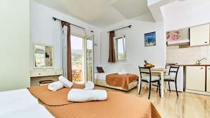 A hotel room with a bed, a desk, a chair, a small table, a window, a balcony, and a kitchenette. - Lotus Studios (Hersonissos)