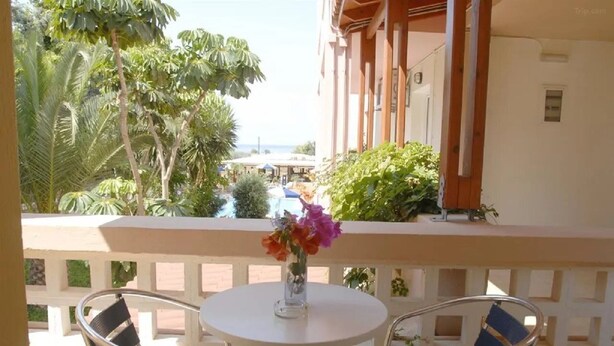 A balcony with a round table and two chairs, overlooking a pool and lush greenery. - Lotus Studios (Hersonissos)