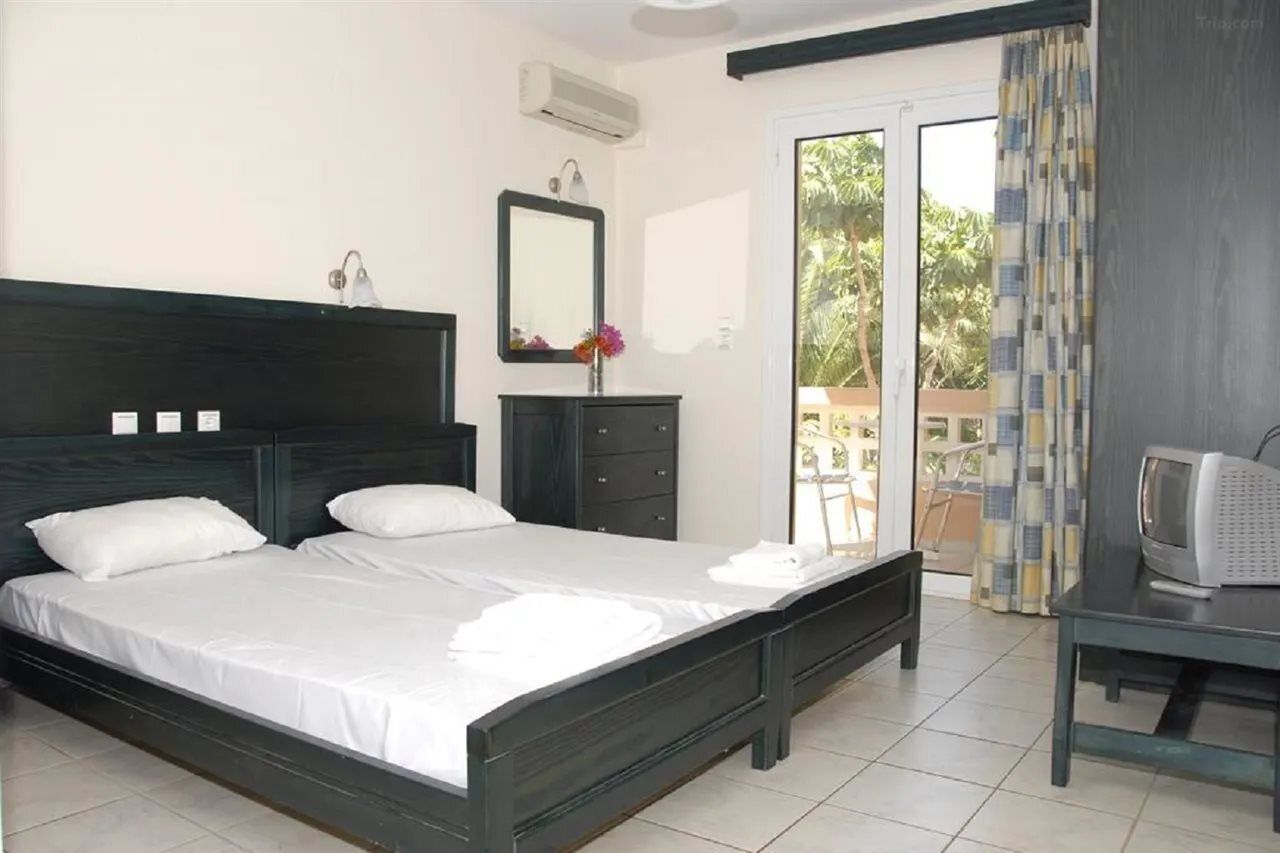 A bedroom with a large bed, a dresser, a TV, and a sliding glass door to a balcony.