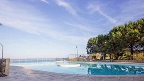 A swimming pool with a clear view of the sea, surrounded by a tiled deck and trees.