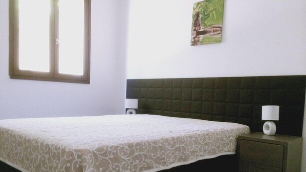 A bedroom with a bed, nightstands, a window, and a wall-mounted picture.