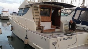 A white yacht named 'U PISCADORU' docked at a marina with other boats.