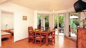 A dining area with a wooden table and chairs, a television mounted on the wall, and a view of the outdoors through glass doors.