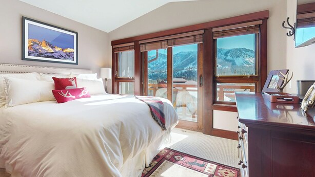 Ein Schlafzimmer mit einem großen Bett, Blick auf Berge durch die Fenster und einer Holzkommode.