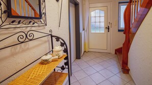 Un couloir avec un escalier, une porte dotée d’une fenêtre et une étagère en métal sur laquelle se trouvent une théière et un bol.