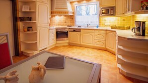 Une cuisine avec des meubles blancs, un four à micro-ondes, une cuisinière et une fenêtre avec des stores.