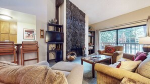 A cozy living room with a stone fireplace, comfortable seating, and a view of the outdoors. - Pet-Friendly, Spacious, Balcony. Near Biking Trails, Pool & Tennis Courts (Mammoth Lakes)