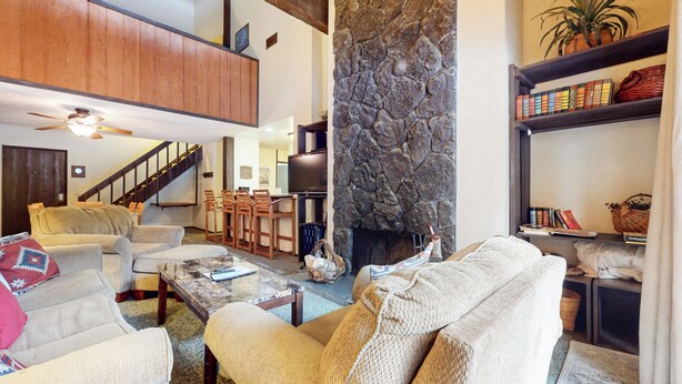 A spacious living room with a stone fireplace, a high ceiling, and a staircase leading to an upper level. - Pet-Friendly, Spacious, Balcony. Near Biking Trails, Pool & Tennis Courts (Mammoth Lakes)
