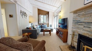 Una sala de estar con sofá, mesa de centro, televisor, chimenea y pared de piedra.
