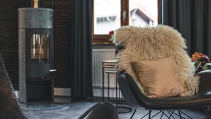 Una habitación acogedora con una chimenea moderna, un sillón mullido y vistas al exterior a través de un ventanal.