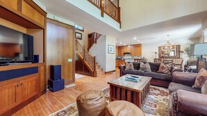 A spacious living room with a large TV, wooden cabinets, a leather sofa, and a staircase leading to an upper level. - Pet-Friendly, Stunning! On Golf Course! Private Hot Tub, Grill, Washer/Dryer (Mammoth Lakes)