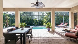 Ein überdachter Patio-Bereich mit Pool, Gartenmöbeln und Topfpflanzen.