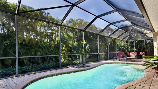 Ein Pool mit Glasumrandung, umgeben von üppiger Vegetation und einer Terrasse mit Sitzgelegenheiten.
