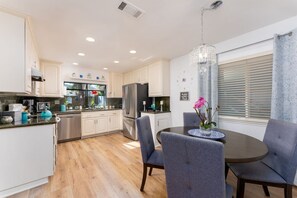 Une cuisine moderne avec des meubles blancs, des appareils en acier inoxydable et un coin repas comprenant des chaises grises et une table.
