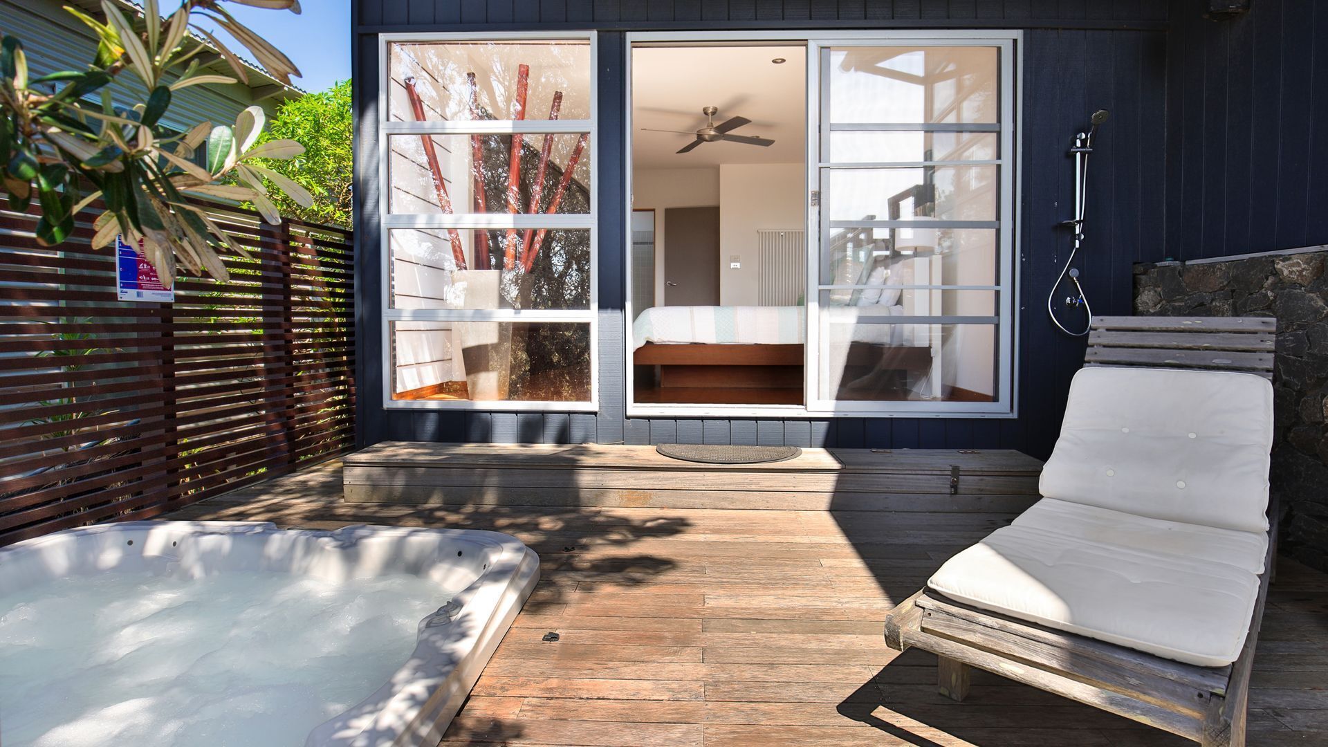 A hot tub and a lounge chair in a backyard with a wooden deck.