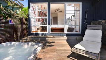 A hot tub and a lounge chair in a backyard with a wooden deck.
