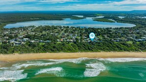 An aerial view of a coastal town with a beach, houses, and a lake. - Illaroo - Absolute Beachfront with Spa (Culburra Beach)