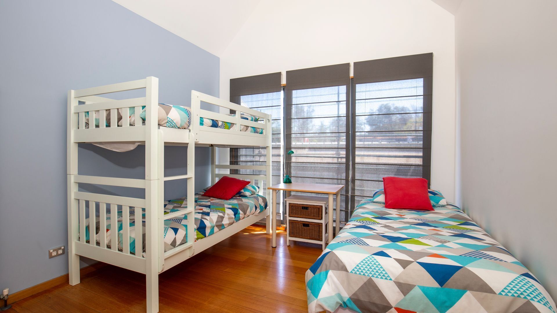 A room with bunk beds, a desk, and a window with blinds.