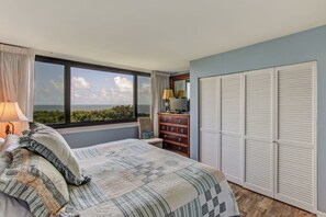 Une chambre avec une grande fenêtre, un lit recouvert d’une courtepointe, une commode et une armoire.