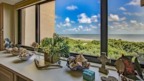 Ein Zimmer mit Blick auf das Meer und den Strand, eine Fensterbank mit Dekoration und eine kleine Statue.