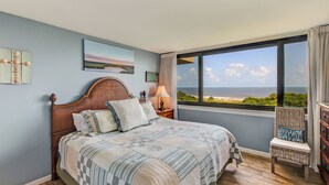Ein Schlafzimmer mit großem Fenster, einem Bett, einem Sessel und einem Nachttisch.