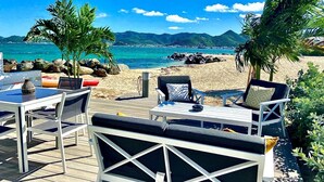 An outdoor seating area with a table and chairs, overlooking a beach and the sea. - Until 6 people, 2 spacious bedrooms, front of the sea, pools tennis parking BBQ (Collectivité de Saint-Martin)