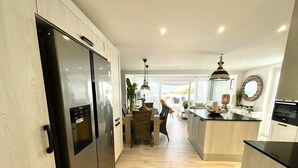 A modern kitchen with stainless steel appliances, a central island, and a dining area with a wicker chair. - Until 6 people, 2 spacious bedrooms, front of the sea, pools tennis parking BBQ (Collectivité de Saint-Martin)
