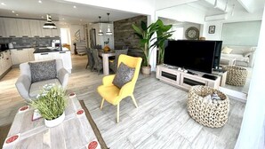 A modern living room with a sofa, armchair, TV, and a dining area with a staircase. - Until 6 people, 2 spacious bedrooms, front of the sea, pools tennis parking BBQ (Collectivité de Saint-Martin)